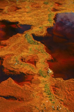 The Rio Tinto in Huelva, Spain, exhibits striking red and orange iron-rich deposits and green microorganism traces