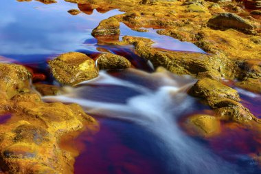 Rich, rust-colored waters of Rio Tinto reflecting the verdant riverside landscape in a serene setting