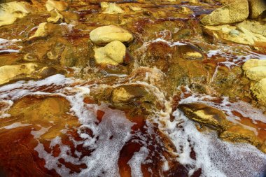 Foaming water rushes over the colorful, iron-laden rocks in the Rio Tinto river