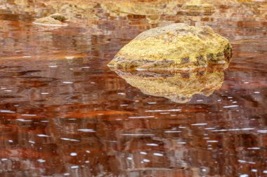 A solitary golden rock casts its reflection upon the tranquil, iron-rich red waters of Rio Tinto