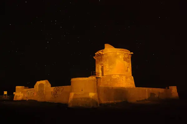 stock image Night view of Torreon de San Miguel del Cabo de Gata bathed in warm light, with a backdrop of the star-studded sky