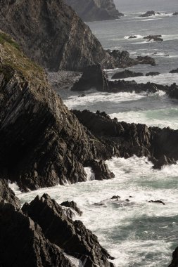 Portekiz, Cabo Sardao 'daki görkemli kayalıklar, engebeli kaya oluşumları ve dalgalar kıyıya çarpıyor. Parçalı bulutlu bir gökyüzü dramatik kıyı manzarasını güçlendirir.
