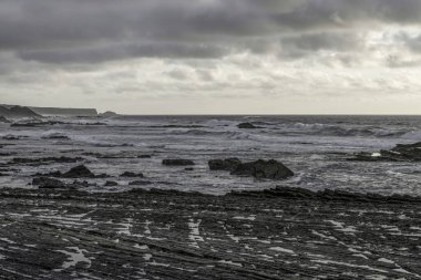 Carriagem Sahili, Portekiz 'de dramatik bulut oluşumlarıyla kasvetli bir gökyüzü. Engebeli kıyı şeridi ve kaya oluşumları alacakaranlıkta çarpıcı ve atmosferik bir manzara yaratır..