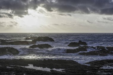 Carriagem Sahili, Portekiz 'de dramatik bulut oluşumlarıyla kasvetli bir gökyüzü. Engebeli kıyı şeridi ve kaya oluşumları alacakaranlıkta çarpıcı ve atmosferik bir manzara yaratır..