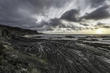 Moody sky with dramatic cloud formations over Carriagem Beach, Portugal. Rugged coastline and rock formations create a striking and atmospheric scene at dusk. clipart