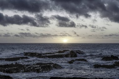 Carriagem Sahili, Portekiz 'de dramatik bulut oluşumlarıyla kasvetli bir gökyüzü. Engebeli kıyı şeridi ve kaya oluşumları alacakaranlıkta çarpıcı ve atmosferik bir manzara yaratır..
