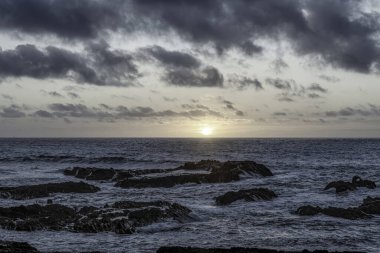 Carriagem Sahili, Portekiz 'de dramatik bulut oluşumlarıyla kasvetli bir gökyüzü. Engebeli kıyı şeridi ve kaya oluşumları alacakaranlıkta çarpıcı ve atmosferik bir manzara yaratır..