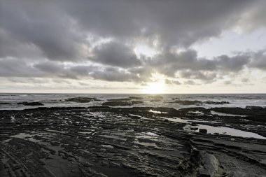 Carriagem Sahili, Portekiz 'de dramatik bulut oluşumlarıyla kasvetli bir gökyüzü. Engebeli kıyı şeridi ve kaya oluşumları alacakaranlıkta çarpıcı ve atmosferik bir manzara yaratır..