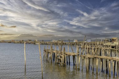Yıpranmış ahşap bir iskele ve küçük bir kulübe yakınlarda demir atmış bir tekneyle sakin bir nehre uzanıyor..