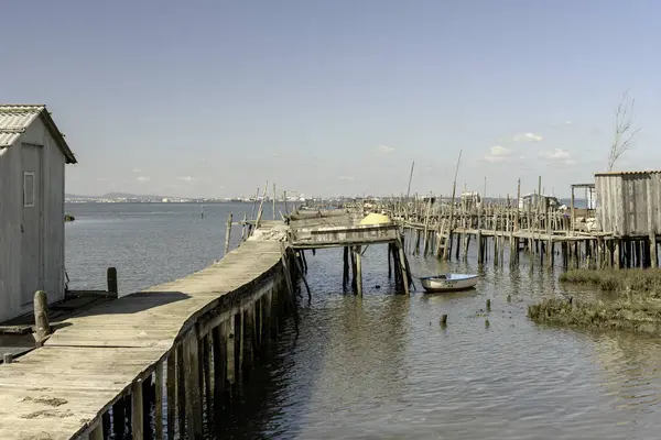 stock image A weathered wooden pier and small hut extend into a tranquil river, with a lone boat anchored nearby.