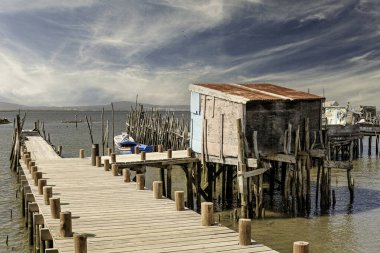 Yıpranmış ahşap bir iskele ve küçük bir kulübe yakınlarda demir atmış bir tekneyle sakin bir nehre uzanıyor..