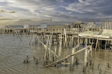 Yıpranmış ahşap bir iskele ve küçük bir kulübe yakınlarda demir atmış bir tekneyle sakin bir nehre uzanıyor..