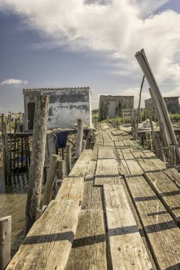 Yıpranmış ahşap bir iskele ve küçük bir kulübe yakınlarda demir atmış bir tekneyle sakin bir nehre uzanıyor..