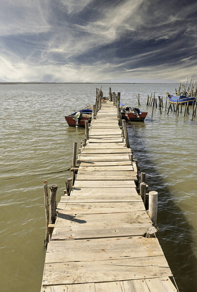 A weathered wooden pier and small hut extend into a tranquil river, with a lone boat anchored nearby.