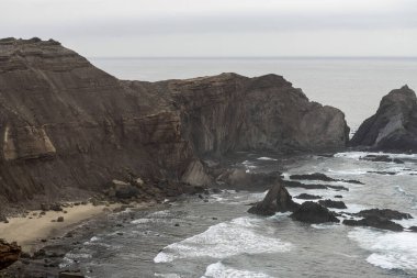 Portekiz Cabo San Vicente 'deki engebeli kayalıkların ve Atlantik Okyanusu manzarası. Benzersiz kaya oluşumları ve sisli atmosfer dramatik bir kıyı manzarası yaratır..
