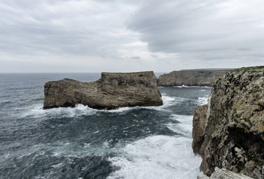 Portekiz Cabo San Vicente 'deki engebeli kayalıkların ve Atlantik Okyanusu manzarası. Benzersiz kaya oluşumları ve sisli atmosfer dramatik bir kıyı manzarası yaratır..