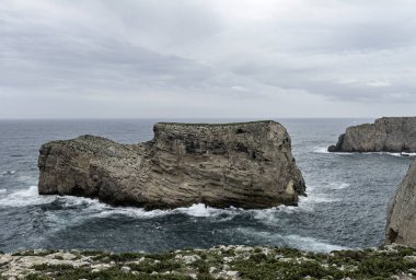 Portekiz Cabo San Vicente 'deki engebeli kayalıkların ve Atlantik Okyanusu manzarası. Benzersiz kaya oluşumları ve sisli atmosfer dramatik bir kıyı manzarası yaratır..