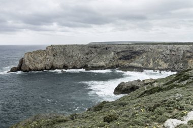 Portekiz Cabo San Vicente 'deki engebeli kayalıkların ve Atlantik Okyanusu manzarası. Benzersiz kaya oluşumları ve sisli atmosfer dramatik bir kıyı manzarası yaratır..