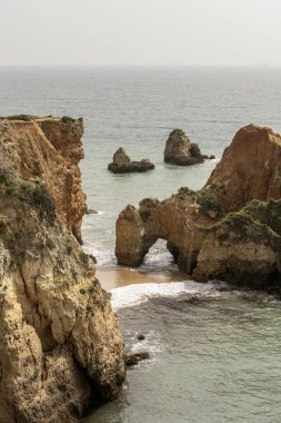 Portekiz 'deki Camilo Sahili' ndeki kayalık kayalıkların ve deniz yığınlarının manzarası. Engebeli kıyı şeridi dramatik kaya oluşumları ve kumlu bir plaja sahiptir..