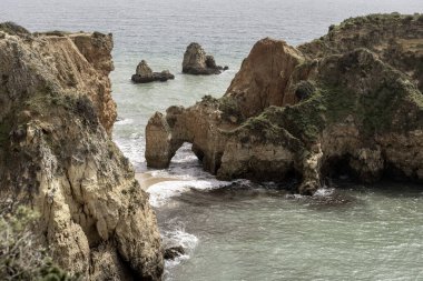 Portekiz, Portimao 'daki kıyı kaya oluşumları ve deniz kemerlerinin çarpıcı görüntüsü. Engebeli kayalıklar ve dağınık deniz yığınları dramatik ve pitoresk bir deniz manzarası yaratır..