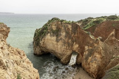 Portekiz, Portimao 'daki kıyı kaya oluşumları ve deniz kemerlerinin çarpıcı görüntüsü. Engebeli kayalıklar ve dağınık deniz yığınları dramatik ve pitoresk bir deniz manzarası yaratır..