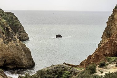 Portekiz, Portimao 'daki kıyı kaya oluşumları ve deniz kemerlerinin çarpıcı görüntüsü. Engebeli kayalıklar ve dağınık deniz yığınları dramatik ve pitoresk bir deniz manzarası yaratır..