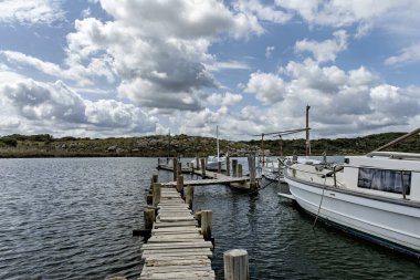 Sanitja Limanı, Menorca 'nın berrak sularına yanaşan teknelere giden ahşap iskele. Parçalı bulutlu bir gökyüzünün altında kayalık kıyı şeridi ve yemyeşil manzarası.