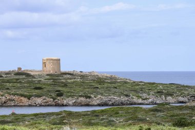 Tarihi Torre de Sanitja, Menorca 'nın sakin sularına bakan engebeli kayalık bir kayanın üzerinde duruyor. Doğal manzara adanın vahşi güzelliğini ve zengin tarihini vurgular..