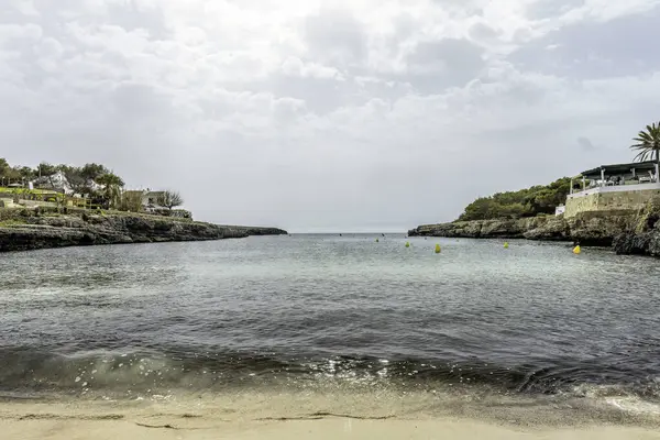 Sakin suları, kayalık uçurumları ve bulutlu gökyüzüyle Menorca 'daki Cala Blanca Sahili' nin huzurlu manzarası. Huzurlu bir kaçış için mükemmel..