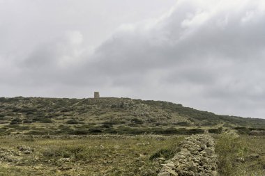 Punta Nati, Menorca 'da geleneksel kuru taş yapıları. Karmaşık taş duvarlar ve yapılar, kır çiçekleriyle benekli doğal manzarayla harmanlanır..