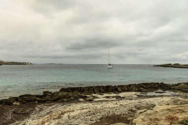 Cala Binibeca, Menorca 'nın kayalık kıyı şeridinde bulutlu bir gökyüzünün altında kırsal bir sahil kulübesi duruyor..