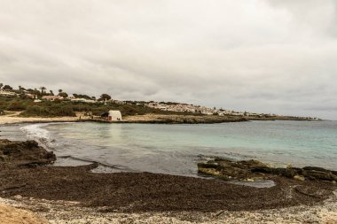 Cala Binibeca, Menorca 'nın kayalık kıyı şeridinde bulutlu bir gökyüzünün altında kırsal bir sahil kulübesi duruyor..
