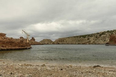 Cala Morell, Menorca 'nın kendine özgü kayalık oluşumları bulutlu bir gökyüzünün altında. Engebeli arazi sakin Akdeniz 'le buluşuyor..