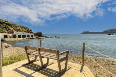 Menorca 'daki Cala des Murtar' ın büyüleyici kıyı köyü, parlak mavi gökyüzünün altında açık ve kayalık kıyı şeridi boyunca kırmızı çatıları olan beyaz evler yer alıyor..