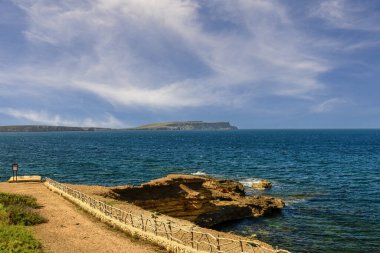 Menorca 'daki Cala Tirant plajının güzel manzarası, berrak mavi sular, kumlu kıyılar ve canlı mavi gökyüzünün altındaki yeşil tepelere kurulmuş beyaz evler..