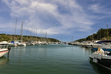 Menorca 'daki Puerto de Addaya Marina' ya yanaşmış, bulutlu bir gökyüzünün altında yemyeşil yemyeşil bir tekne ve yat manzarası..