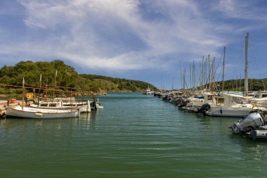 Menorca 'daki Puerto de Addaya Marina' ya yanaşmış, bulutlu bir gökyüzünün altında yemyeşil yemyeşil bir tekne ve yat manzarası..