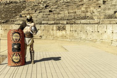 A reenactor dressed as a Roman gladiator poses with a shield and helmet in the ancient amphitheater of Merida, Spain. clipart