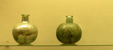 Karmaşık dizaynlı antik bir Roma yeşil cam vazosu. Geniş bir vücudu, dar bir boynu ve dekoratif kulpları var. Roma cam işçiliği sergiliyor..