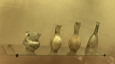 Karmaşık dizaynlı antik bir Roma yeşil cam vazosu. Geniş bir vücudu, dar bir boynu ve dekoratif kulpları var. Roma cam işçiliği sergiliyor..