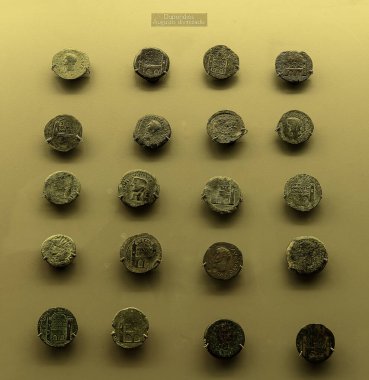 Bir müze sergisinde sergilenen sunak tasarımı içeren antik Roma sikkeleri koleksiyonu. Roma dini ve kültürel sembolizminin gösterimi.