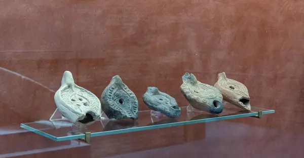 stock image A diverse collection of ancient Roman oil lamps exhibited on a red background. These artifacts showcase intricate designs and craftsmanship from the Roman era, each telling a unique historical story.