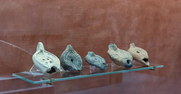 Stock image A diverse collection of ancient Roman oil lamps exhibited on a red background. These artifacts showcase intricate designs and craftsmanship from the Roman era, each telling a unique historical story.