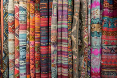 Bir pazarda karmaşık desenler sergilenen renkli katlanmış kumaş yığını, canlı renkler ve işçilik sergiliyor..