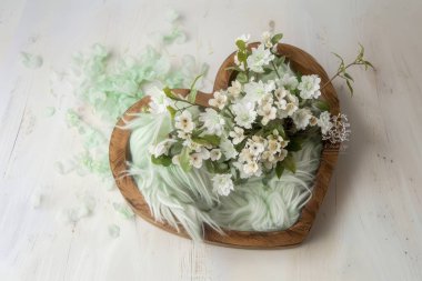 Beyaz çiçekli kalp şeklinde ahşap bir kase ve açık arkaplanda yumuşak yeşil bir kumaş..