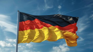 The German national flag waving in the wind with a bright, clear sky in the background.