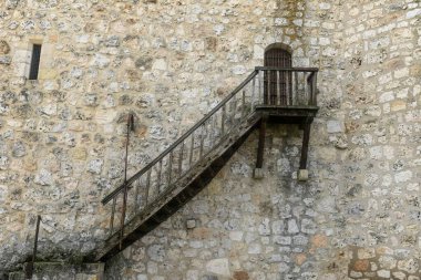 A close-up of Torija Castle's stone wall, featuring a wooden staircase leading to a small gated window, showcasing medieval architectural details. clipart