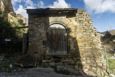 A beautifully aged wooden door framed by a stone arch, set within a rustic stone wall in the village of Fanlo, Huesca. clipart