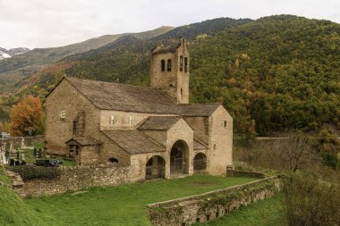 Çan kulesi ve kemerli portosu olan antik taş kilise ormanlık tepeleri olan huzurlu bir kırsal alana kurulmuş..