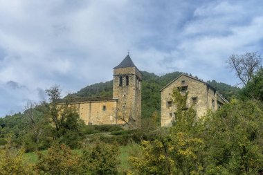 Bir saati ve kemerli girişi olan uzun taş çan kulesi, yeşilliklerle çevrili ve parlak mavi gökyüzüne karşı kurulmuş..